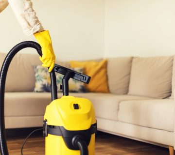 Woman cleaning sofa with yellow vacuum cleaner. Copy space. Cleaning service concept